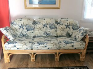 Rattan sofa with all loose pleated cushions for a seasonal cottage on Cape Cod | Upholstered in an indoor-outdoor beach theme fabric | Upholstered by Cape Cod Upholstery Shop | Located in South Dennis, MA 02660