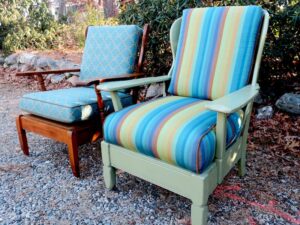 Two Cape Cod cottage style maple chairs from the side view. One stained in a natural maple finish and the other painted sage green | Upholstered with both an indoor-outdoor blue diamond pattern fabric and Sunbrella multi colored stripe | Upholstered by Cape Cod Upholstery Shop | Located in South Dennis, MA 02660