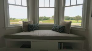 Large Plush 105"x32" trapezoid window seat cushion for a home with a golf course view and close to the South Cape Beach State Park | Cushion cover fabricated with Sunbrella Hybrid Smoke. Cushion Insert fabricated with a foam core wrapped in a down/feather envelope | Cushions fabricated by Cape Cod Upholstery Shop | Located in South Dennis, MA 02660