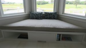 Large Plush 105"x32" trapezoid window seat cushion for a home with a golf course view and close to the South Cape Beach State Park | Cushion cover fabricated with Sunbrella Hybrid Smoke. Cushion Insert fabricated with a foam core wrapped in a down/feather envelope | Cushions fabricated by Cape Cod Upholstery Shop | Located in South Dennis, MA 02660