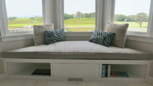 Large Plush 105"x32" trapezoid window seat cushion for a home with a golf course view and close to the South Cape Beach State Park | Cushion cover fabricated with Sunbrella Hybrid Smoke. Cushion Insert fabricated with a foam core wrapped in a down/feather envelope | Cushions fabricated by Cape Cod Upholstery Shop | Located in South Dennis, MA 02660