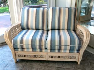 Rattan love seat shown in the clients three season room. Upholstered in a Sunbrella Scope Cape stripe fabric | Upholstered by Cape Cod Upholstery Shop | Located in South Dennis, MA 02660
